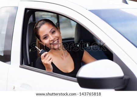 happy young woman showing a car key inside her just bought new vehicle