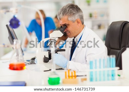 senior medical researcher looking through the microscope with colleagues on background
