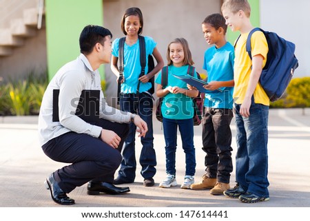cute elementary pupils outside classroom talking to teacher