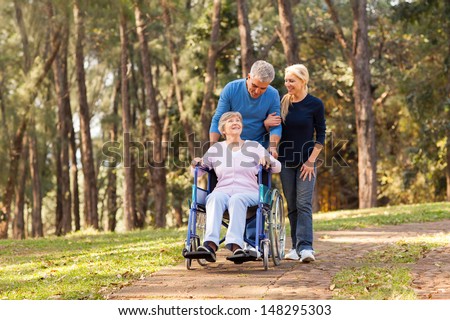 caring couple taking their disable senior mother for a walk at the park