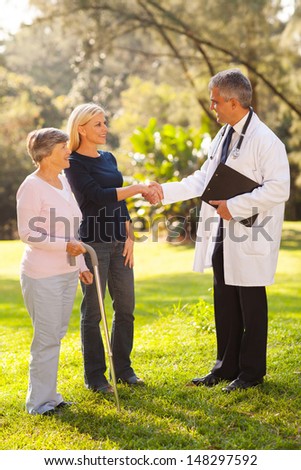 mature retirement village doctor greeting senior patient\'s daughter outdoors