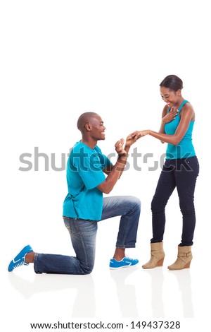 African man putting engagement ring on his excited girlfriend after she said yes isolated on white