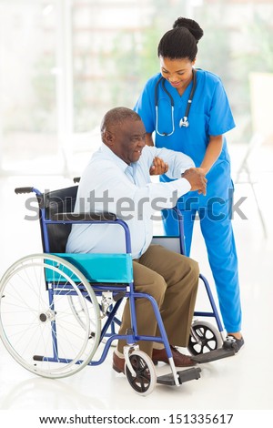friendly african caregiver helping senior man getting up from wheelchair