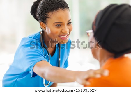 caring african medical nurse comforting senior patient in office