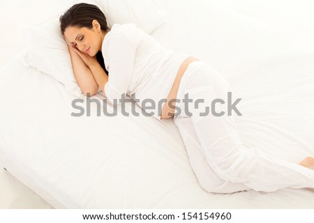 overhead view of cute pregnant woman sleeping on bed