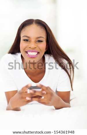 cheerful african american woman using cell phone lying on bed