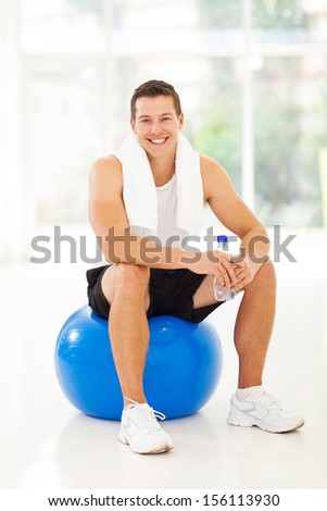 cheerful young man sitting on gym ball, holding water bottle