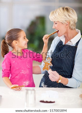 cute little girl feeding just baked gingerbread cookies to her grandmother