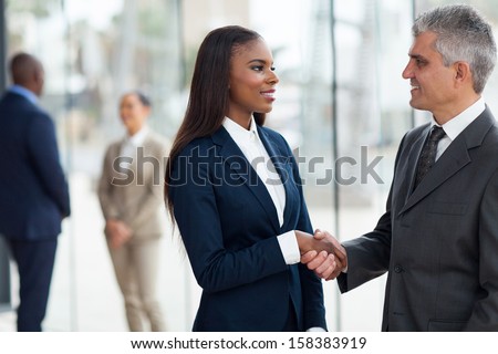 friendly senior businessman handshaking with young businesswoman in office