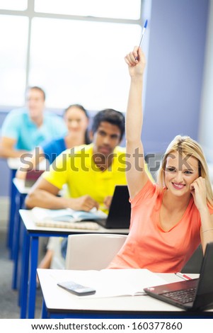 beautiful female university student raising her hand to ask a question in lecture room