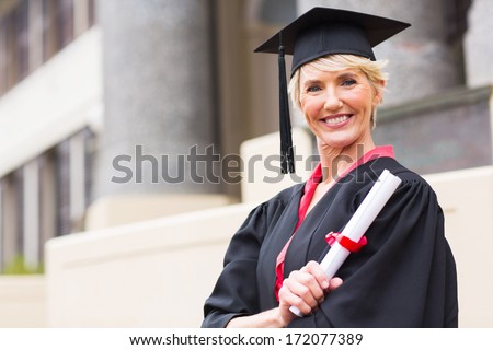 happy middle aged woman with graduation cap and gown holding diploma