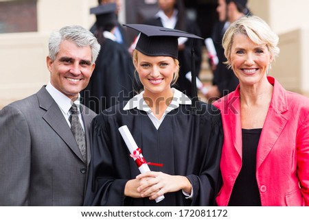 smiling young female graduate with parents at graduation ceremony