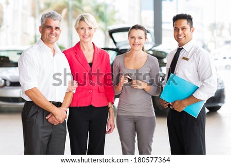 family of three standing with salesman at vehicle dealership after buying a new car
