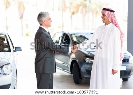 smiling middle aged car dealer handshake with arabian man