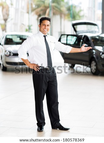 good looking indian car salesman standing at showroom presenting new cars