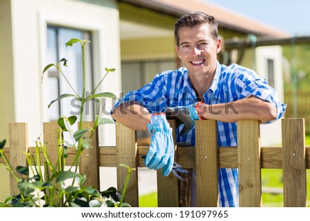 young man leaning against fence relaxing after doing some garden work in backyard