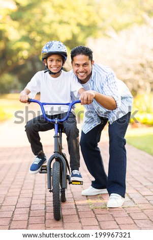 happy little indian boy learning to ride a bike with help of his father