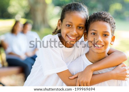 cheerful little indian sister and brother standing in front of parents in the park