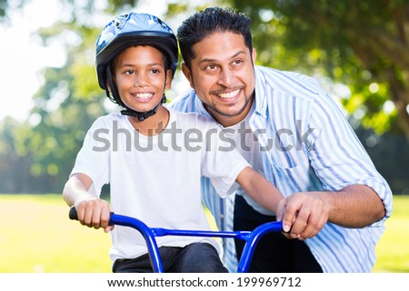 cheerful indian man helping his son to ride a bike in forest