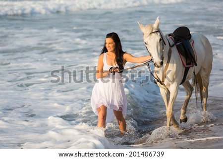smiling young woman walking with a white horse on beach