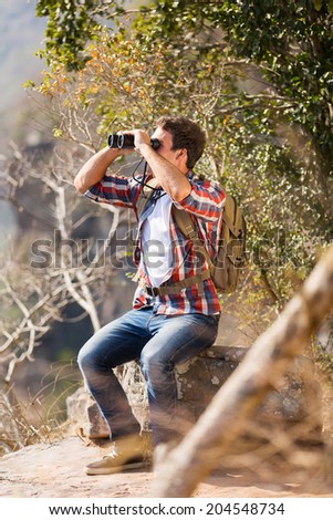 young man sitting on top of the mountain and using binoculars