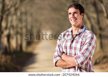 happy young man with arms crossed on autumn country road