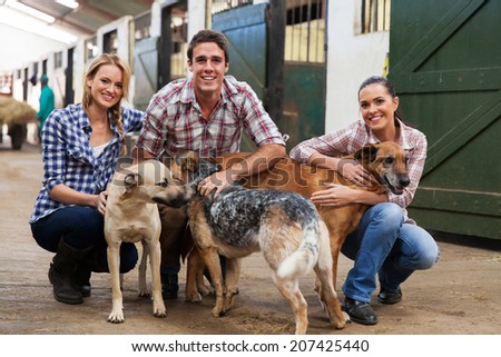 group of happy farm workers with pet dogs in stables