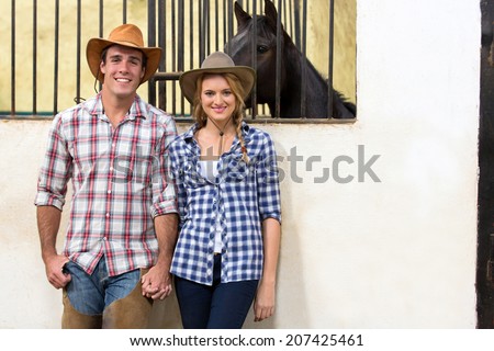 happy cowboy and cowgirl couple holding hands inside stables