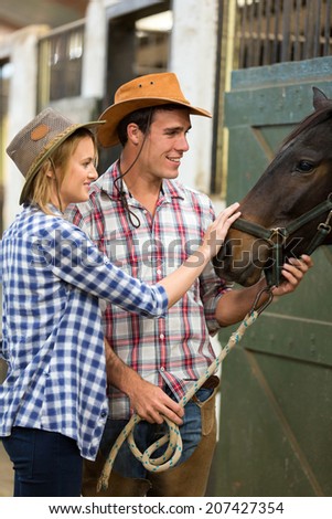 caring cowboy and cowgirl in stable touching a horse