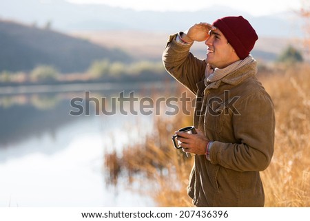 happy young man holding coffee mug and looking into distance in winter morning
