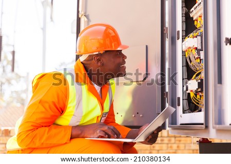 experienced african electrician checking computerized machine status with laptop