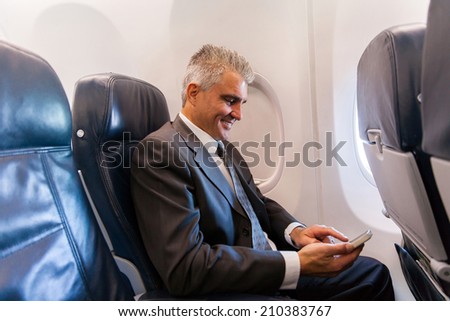 happy middle aged businessman using cell phone on airplane
