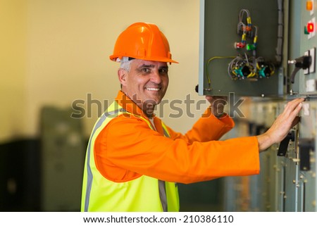 happy mid age electrician checking industrial control box