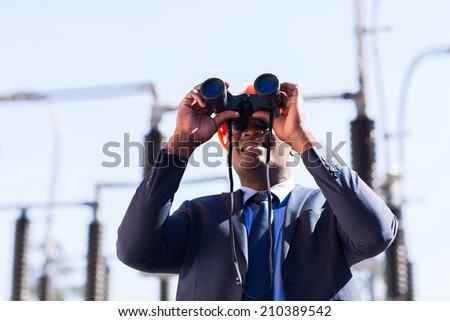 african american electrical manager using binoculars looking at substation