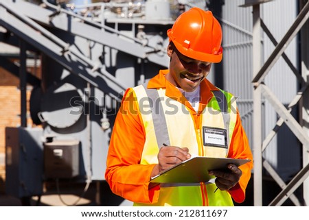 happy african electrician writing on clipboard in electric substation