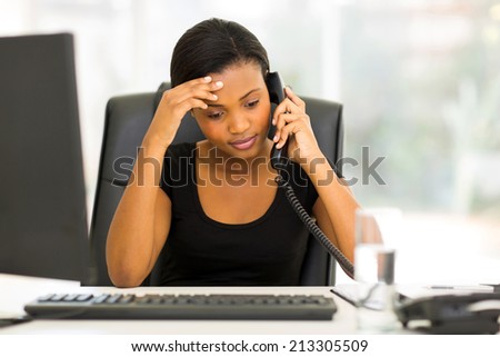 tired black businesswoman using landline phone in office