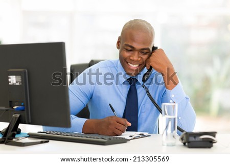 happy african businessman talking on landline phone and writing report