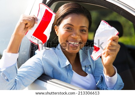 happy african female driver tearing up her L sign sitting in a car
