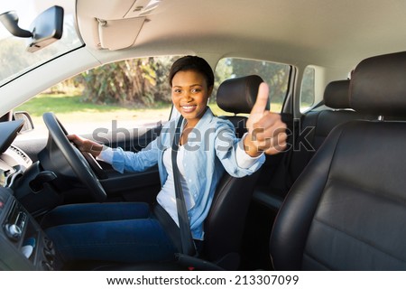 attractive young african female driver giving thumb up inside her new car