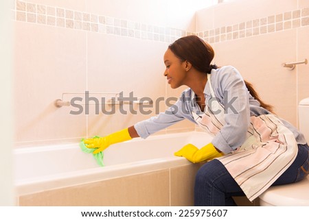 young african housewife cleaning up bathtub at home