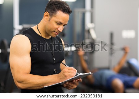 muscular mid age male gym trainer writing on clipboard