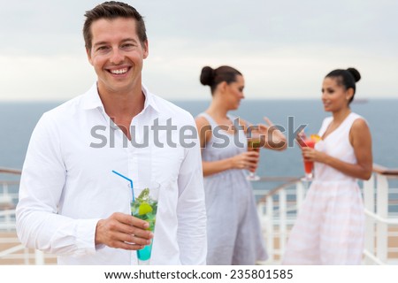 happy young man holding cocktail drink with friends on background on a cruise ship