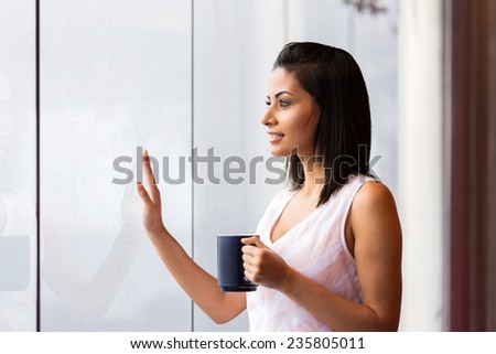 thoughtful woman standing next to the window with coffee mug