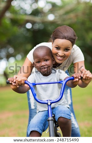 beautiful african mother teaching her little son to ride a bike at the park
