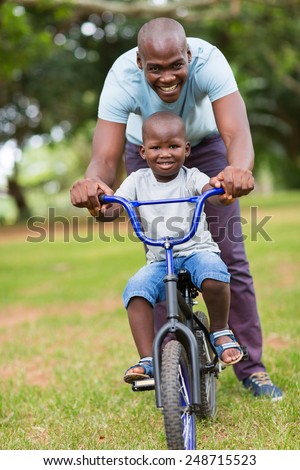 cheerful african american man teaching son to ride a bicycle at the park