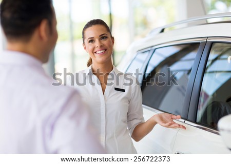attractive saleswoman showing new car to a customer in showroom
