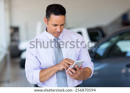 mid age car salesman using cell phone in showroom