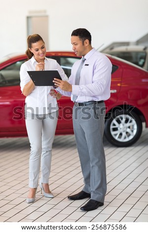 car dealer explaining sales contract to young woman buying a car