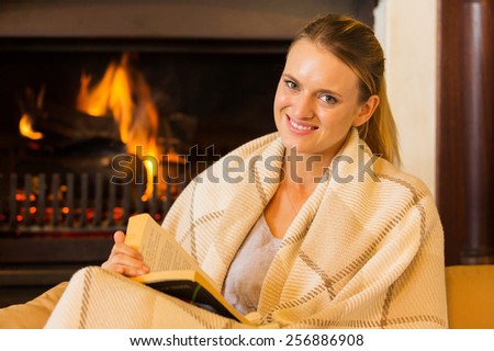 attractive woman sitting near fireplace at home reading book