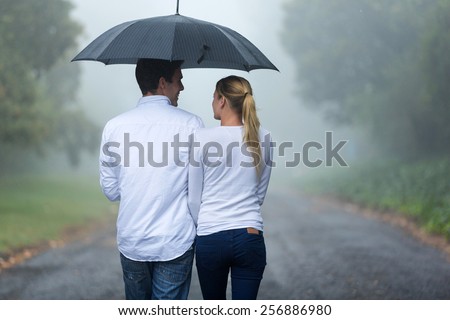 rear view of romantic couple walking in rain